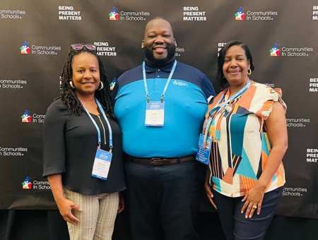 CIS of Baytown's Program Director and Executive Director standing beside Alumnus Malik with a black backdrop featuring the CIS logo
