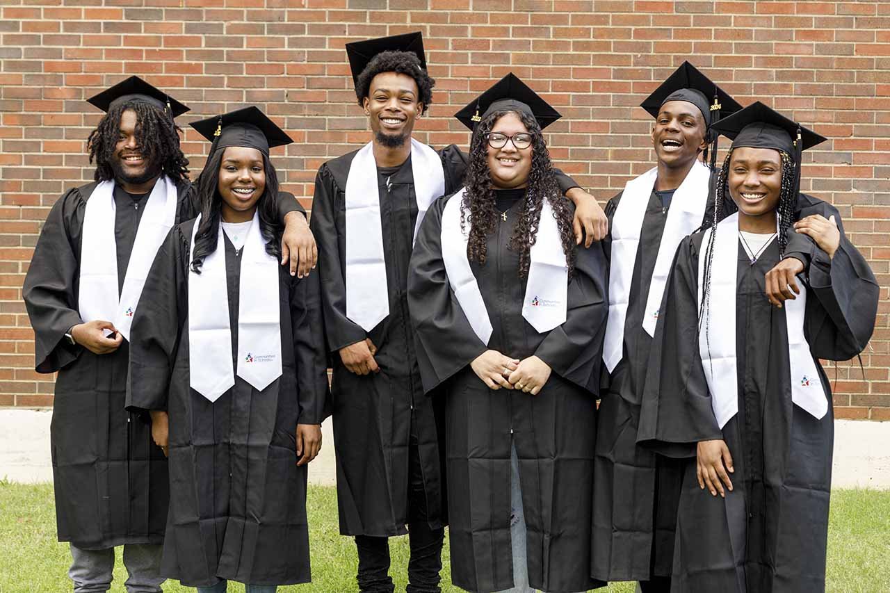 students standing in their cap and gowns outside in front of a brick wall