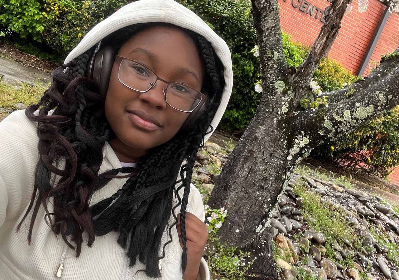 Student wearing glasses, headphones and a hoodie outside